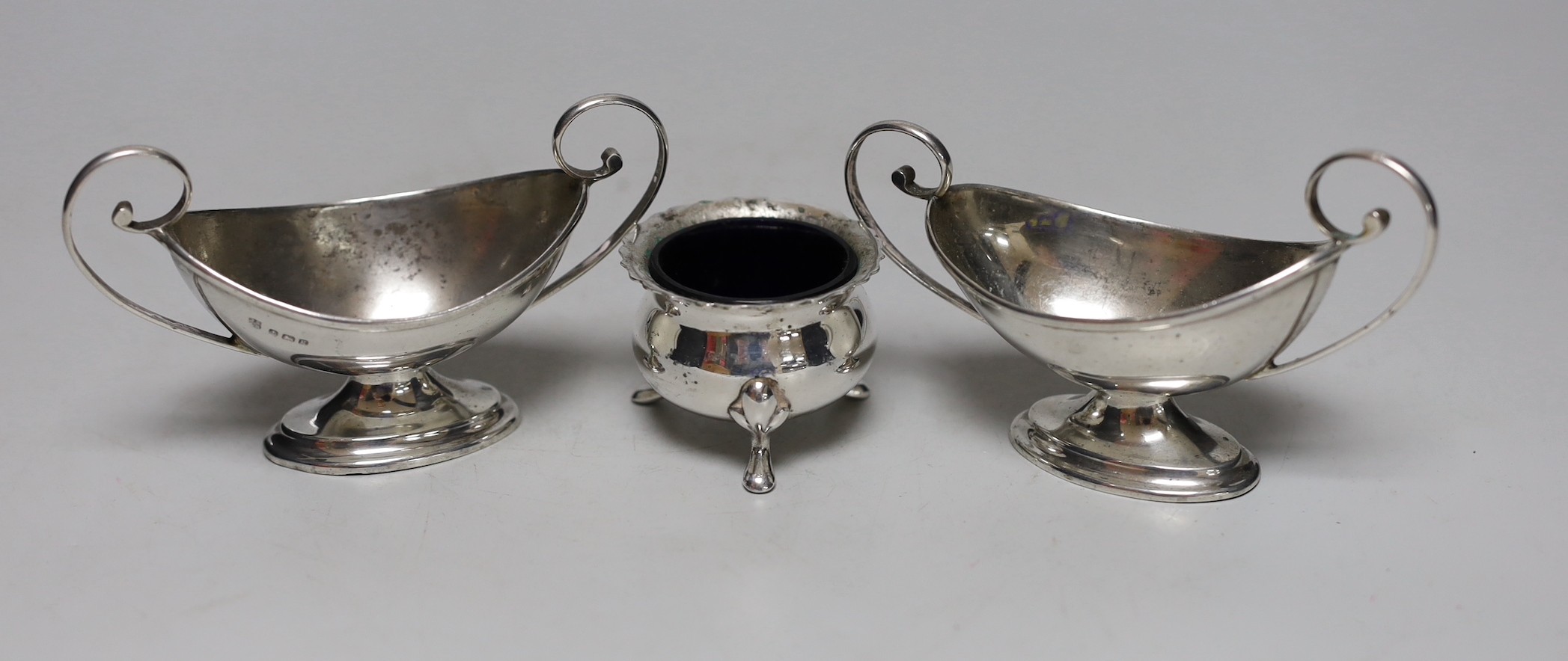 A pair of George V silver two handled boat shaped pedestal salts length 10.7cm, a pair of Edwardian silver pepperettes, a pair of late Victorian silver menu holders, a pair of silver sugar tongs and a three piece plated